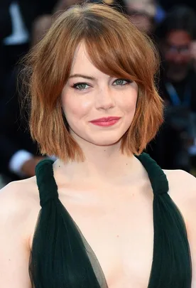 A woman with a short auburn bob haircut, wearing a green dress, smiles at a formal event.