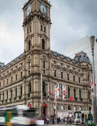 Exterior of H&M store in a historic building with a clock tower in Sydney, with tram and people in front.