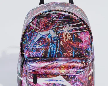 A multicolored, abstract-patterned backpack with a front pocket and a black handle on top against a plain background.