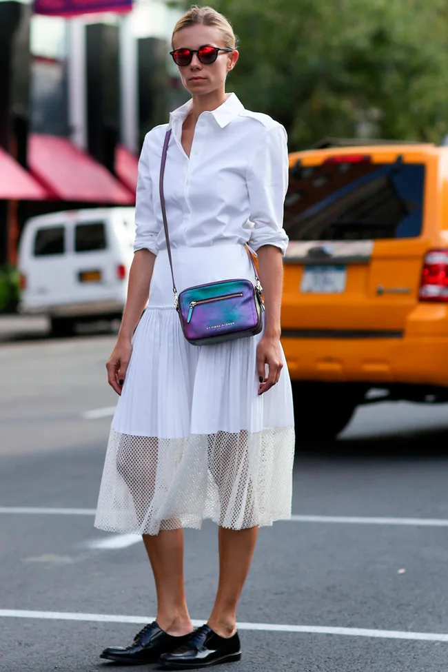 Woman in white dress and red sunglasses, with a purple crossbody bag, stands in front of a yellow taxi in a city street.