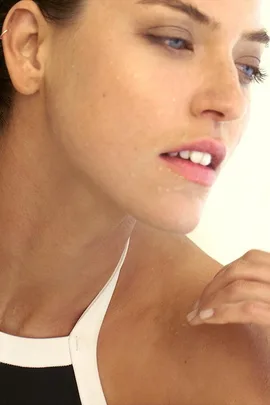 Close-up of a woman with wet skin wearing a black and white swimsuit, looking to the side with a thoughtful expression.