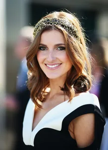 Woman with wavy hair wearing a decorative headband and a black-and-white dress, smiling outdoors.