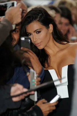 Woman in black and white dress poses for selfies with fans in a crowded setting.