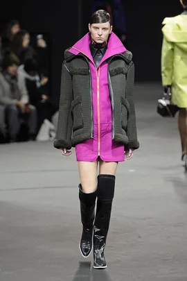 Model on runway in a pink and black outfit with a puffer jacket, knee-high boots, and slicked-back hair.