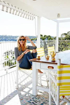 Cheyenne Tozzi sits on a bright terrace in Sydney, featuring yellow striped chairs and a view of lush greenery.