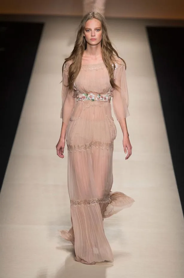 Model wearing a flowing, sheer beige gown with floral detailing, walking on a runway at Alberta Ferretti SS15 fashion show.