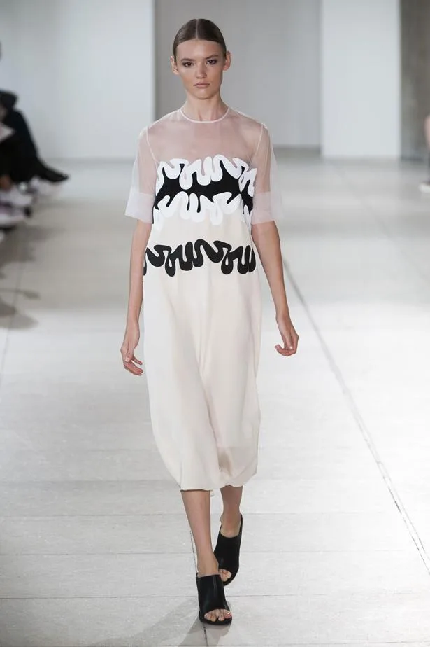 Model walks runway in a sheer top dress with black and white wavy design during Spring/Summer fashion show.