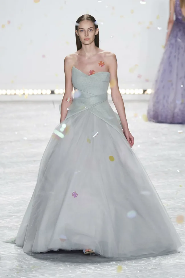 Model in a strapless, light grey gown with tulle skirt walking runway, floral appliqués on bodice, Monique Lhuillier SS15.