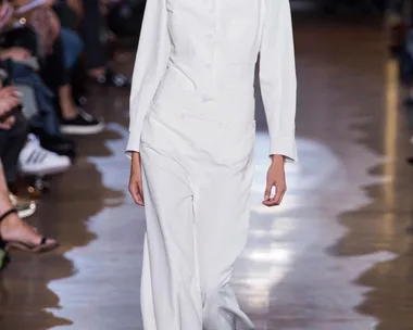 Model walking in Stella McCartney Spring/Summer 2015 show wearing a white tailored suit on a wooden runway.