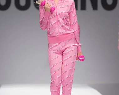 Model in pink Moschino tracksuit and headband walks runway holding pink weights during the Moschino SS15 fashion show.