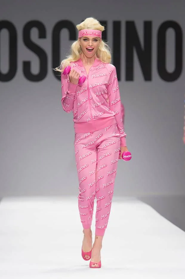 Model in pink Moschino tracksuit and headband walks runway holding pink weights during the Moschino SS15 fashion show.