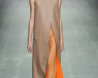 Model walking the runway in a sleeveless tan coat and sheer orange pants at Lucas Nascimento SS15 fashion show.