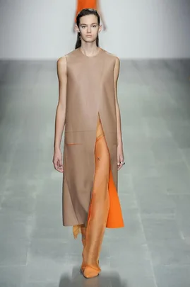 Model walking the runway in a sleeveless tan coat and sheer orange pants at Lucas Nascimento SS15 fashion show.