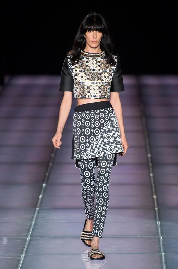 Model walks runway in Fausto Puglisi SS15 outfit with geometric patterns, black hair, and flat sandals.