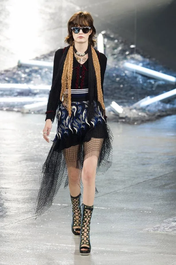 Model on runway wearing eclectic Rodarte SS15 outfit with fringe details, mesh, sunglasses, and lace-up sandals.