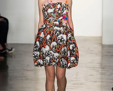 Model on runway wearing a dress with skull and flame design, floral headpiece, and black boots.