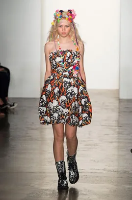 Model on runway wearing a dress with skull and flame design, floral headpiece, and black boots.