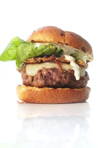 A close-up of a gourmet burger with lettuce, cheese, crispy onions, and sauce, served on a toasted bun.