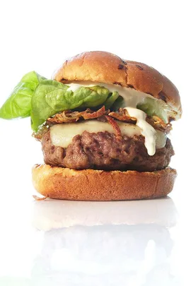 A close-up of a gourmet burger with lettuce, cheese, crispy onions, and sauce, served on a toasted bun.