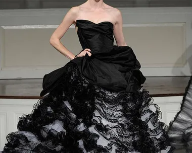 A model walks the runway in an elegant, strapless black Oscar de la Renta gown with ruffled layers and lace details.