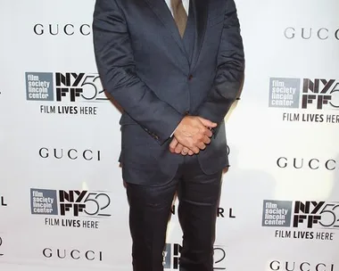 Man in a dark suit posing on a red carpet at an event with a "Gone Girl" backdrop.