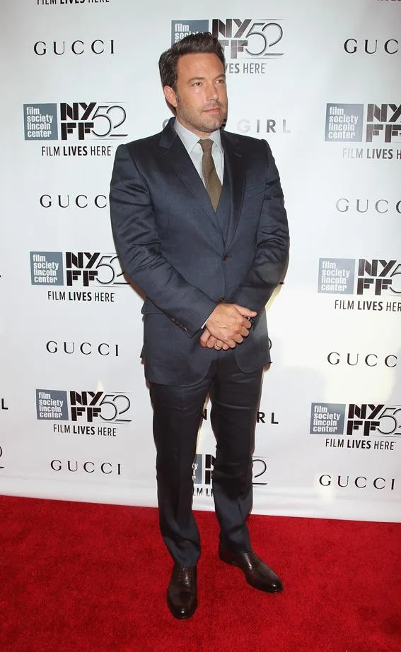 Man in a dark suit posing on a red carpet at an event with a "Gone Girl" backdrop.