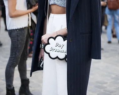 A person in a navy coat holds a cloud-shaped bag with "Day Dreamer" text at a street fashion event.