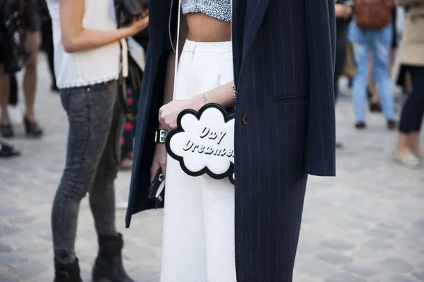 A person in a navy coat holds a cloud-shaped bag with "Day Dreamer" text at a street fashion event.