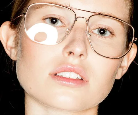 Close-up of a person wearing large, thin-framed glasses with a bright reflection on one lens.