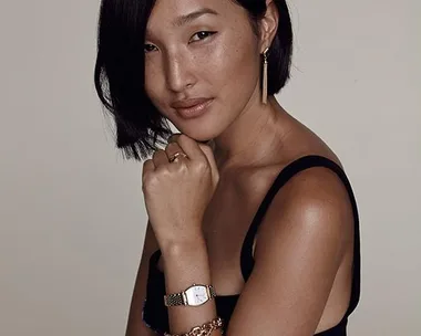 Nicole Warne poses with jewelry and a watch against a plain backdrop, wearing a sleeveless top.