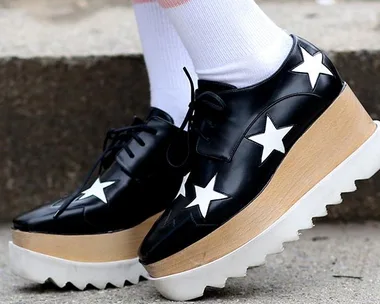 Black platform shoes with white stars and striped socks on a concrete surface.