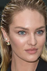 Close-up of a woman with blue eyes, natural makeup, wet hair, and multiple earrings, including pearls.