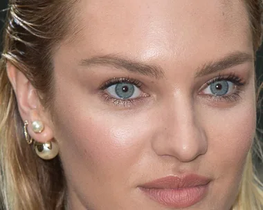 Close-up of a woman with blue eyes, natural makeup, wet hair, and multiple earrings, including pearls.