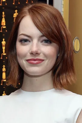 Emma Stone smiling at an event, wearing a white top, with a patterned background.