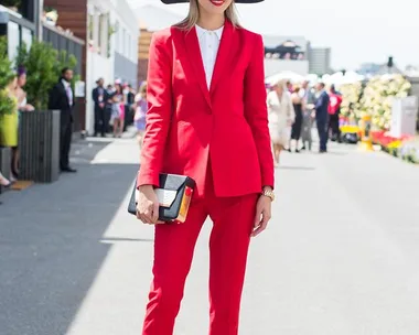 Woman in a bright red suit and a wide-brimmed hat, standing stylishly at Oaks Day event.