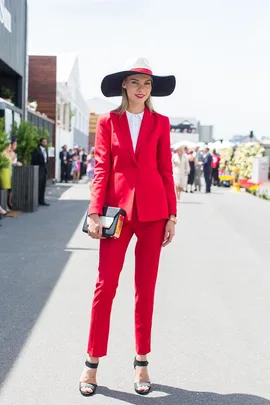 Woman in a bright red suit and a wide-brimmed hat, standing stylishly at Oaks Day event.