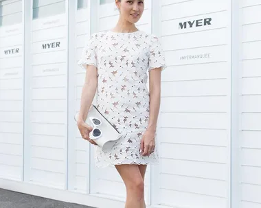 Woman in white lace dress and nude hat poses at Emirates Stakes Day 2014, holding a white clutch.