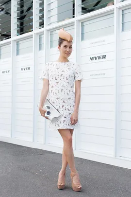 Woman in white lace dress and nude hat poses at Emirates Stakes Day 2014, holding a white clutch.