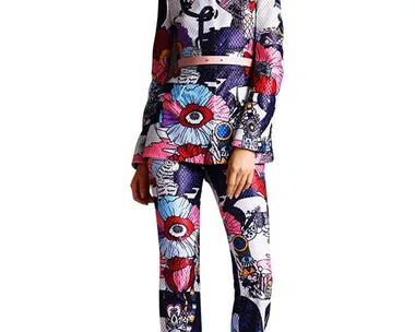 Model in a colorful, cartoon-print pantsuit with floral and abstract designs, posing confidently on a white background.