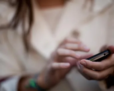 Close-up of a person in a white shirt using a smartphone, typing on the screen with both hands.