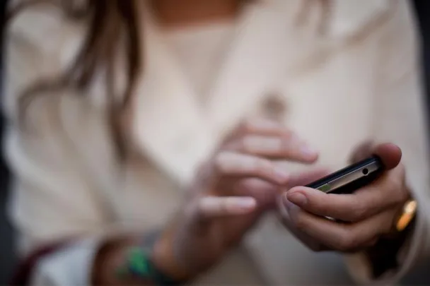 Close-up of a person in a white shirt using a smartphone, typing on the screen with both hands.