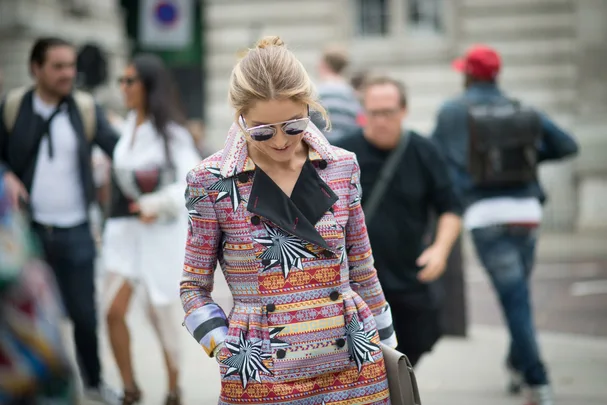 Fashionably dressed woman in a vibrant patterned coat walking on the street, wearing sunglasses.