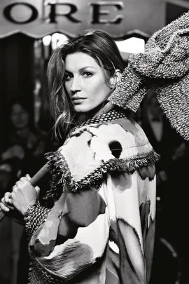 Black and white image of a woman in a fringed coat holding a textured bag, with "ORE" sign partially visible in the background.