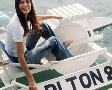 A woman in a white tee and jeans smiling while sitting on a paddle boat near water, with "CARLTON" on the side.