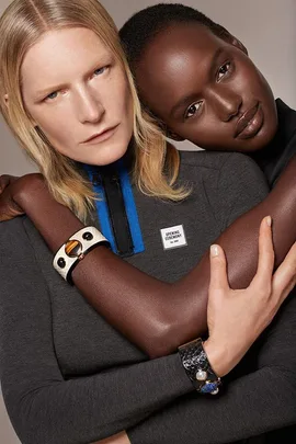 Two models embracing, wearing geometric jewelry and a knit top with a label that says "Opening Ceremony."