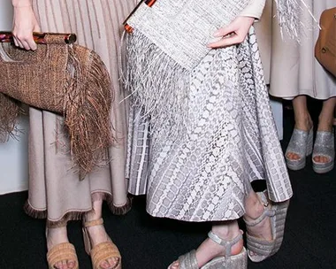 Fashionable individuals in textured, neutral dresses holding woven and fringed clutches, wearing platform sandals.