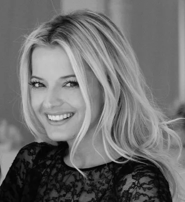 A woman with long blonde hair, smiling and wearing a lacy black top. Black and white photo.