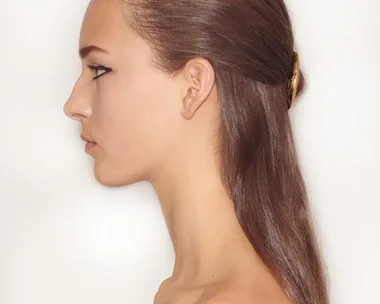 Profile of a person with slicked-back hair, held by a golden hair accessory, on a neutral background.