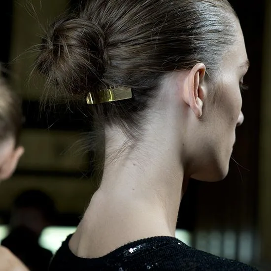 Profile of a woman with hair in a bun, secured by a gold clip, wearing a black sequined top.