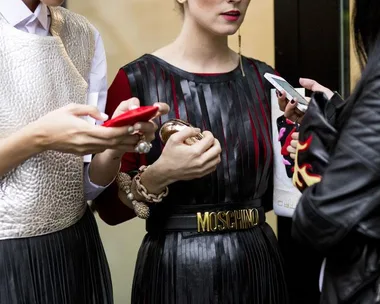 People wearing fashionable outfits, including a Moschino belt, and using smartphones while standing together.